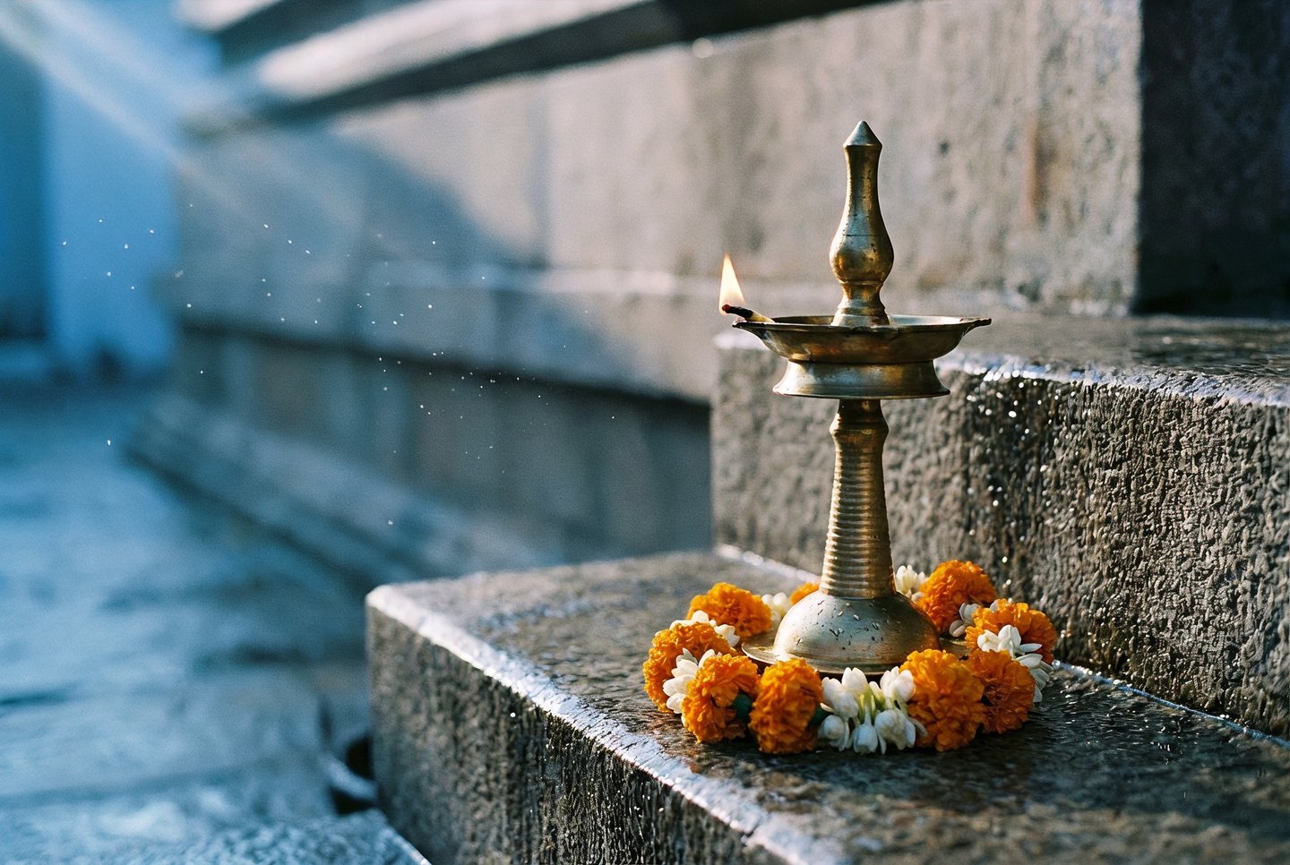 Brass oil lamp with burning flame adorned by marigold garland on ancient stone temple steps in sunlight.