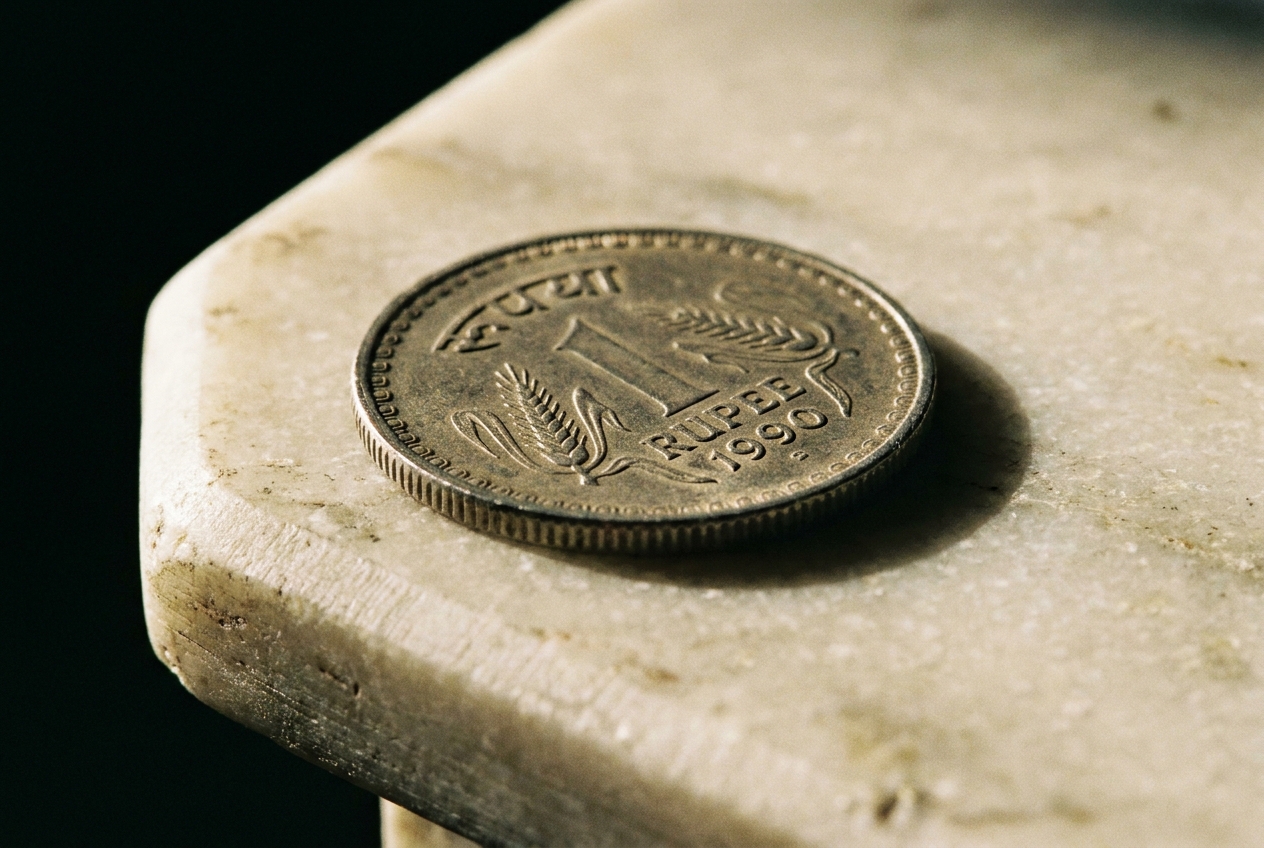 Macro view of a 1990 Indian one rupee coin resting on a beveled marble tabletop edge.