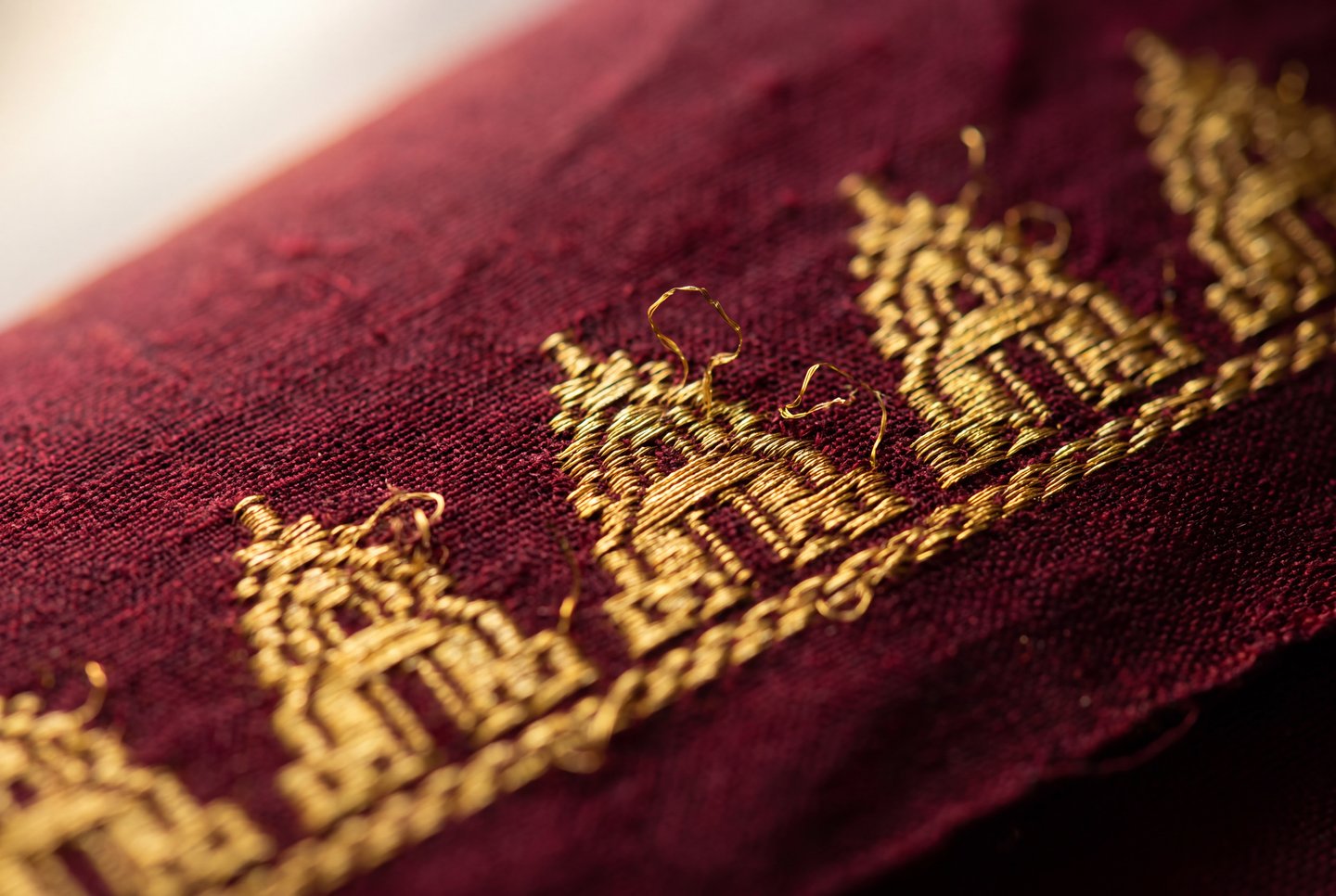 Gold metallic embroidered temple motifs stand out in close-up against textured crimson silk fabric.
