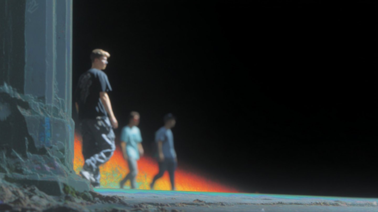 Three young men walk in a line against a black void with vibrant thermal-colored light trails.