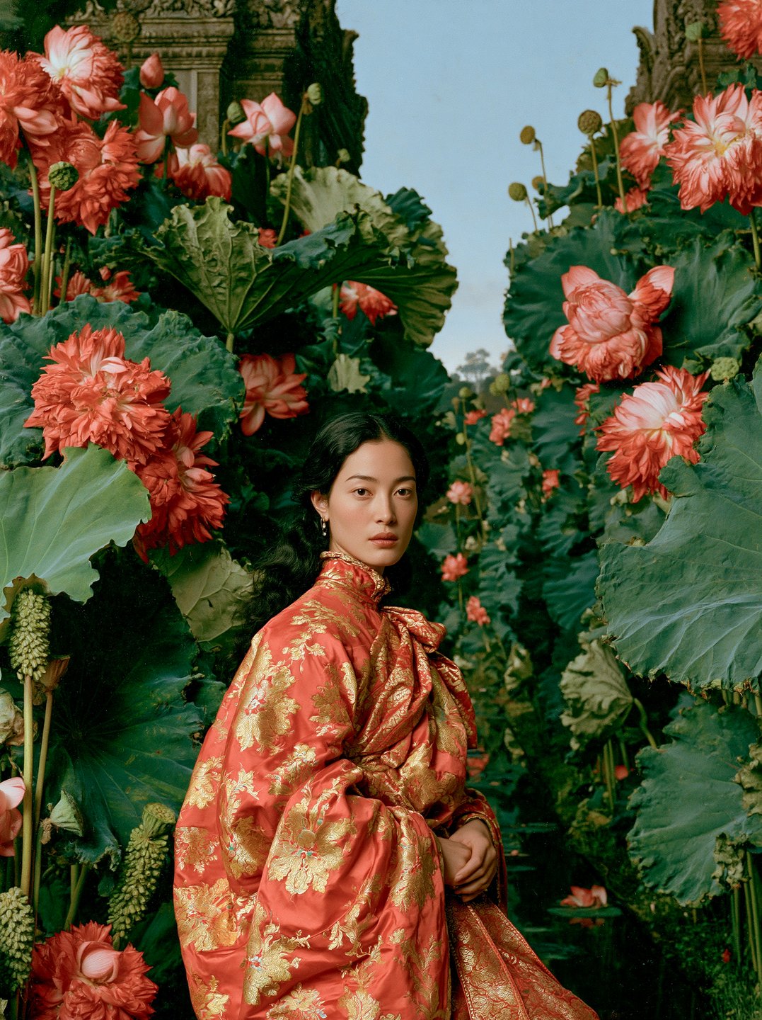 Serene woman wearing an ornate red and gold brocade dress stands surrounded by giant red lotus blossoms.