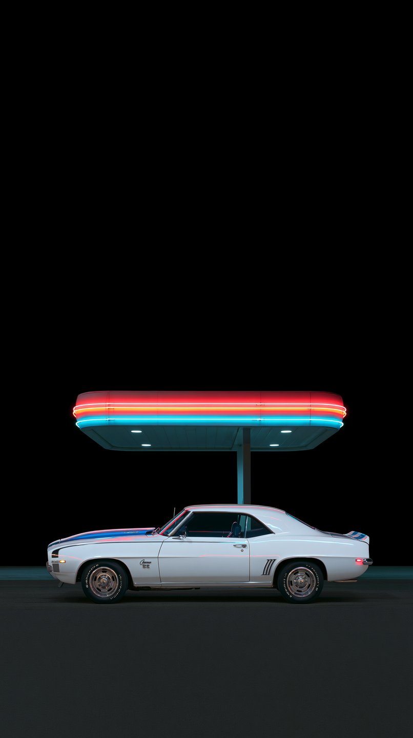 White vintage muscle car parked under a red and blue neon canopy against a solid black background.