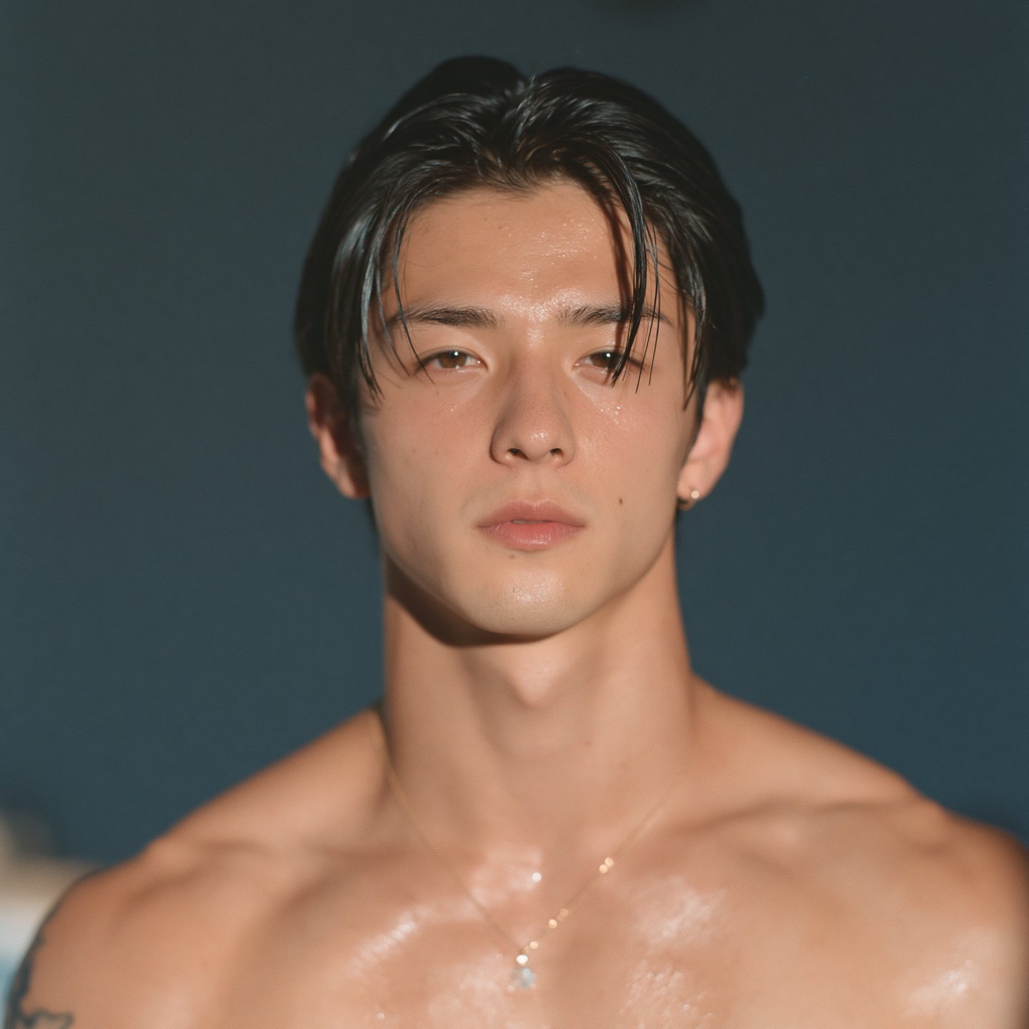 Close-up portrait of a young man with wet hair and glistening skin against a dark background.
