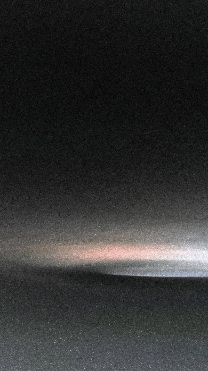 A dark, grainy abstract composition featuring a soft horizontal streak of pink and white light.