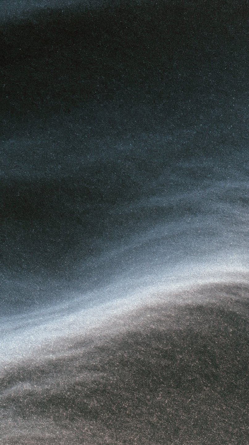 A tiny solitary figure stands on the sweeping ridge of vast, textured dark sand dunes.