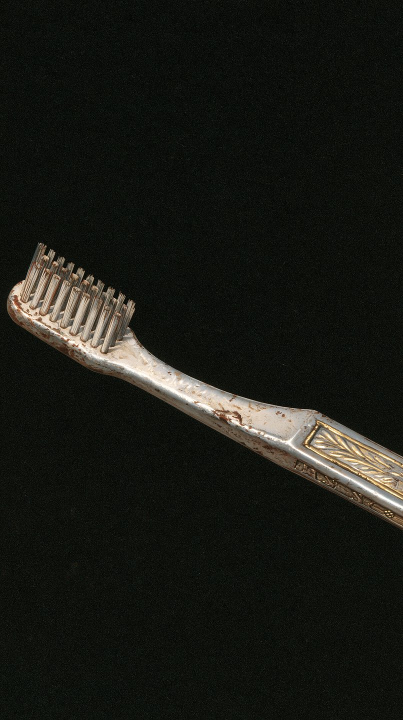 Ornate antique toothbrush with gilded details and silver handle set against a solid black background.