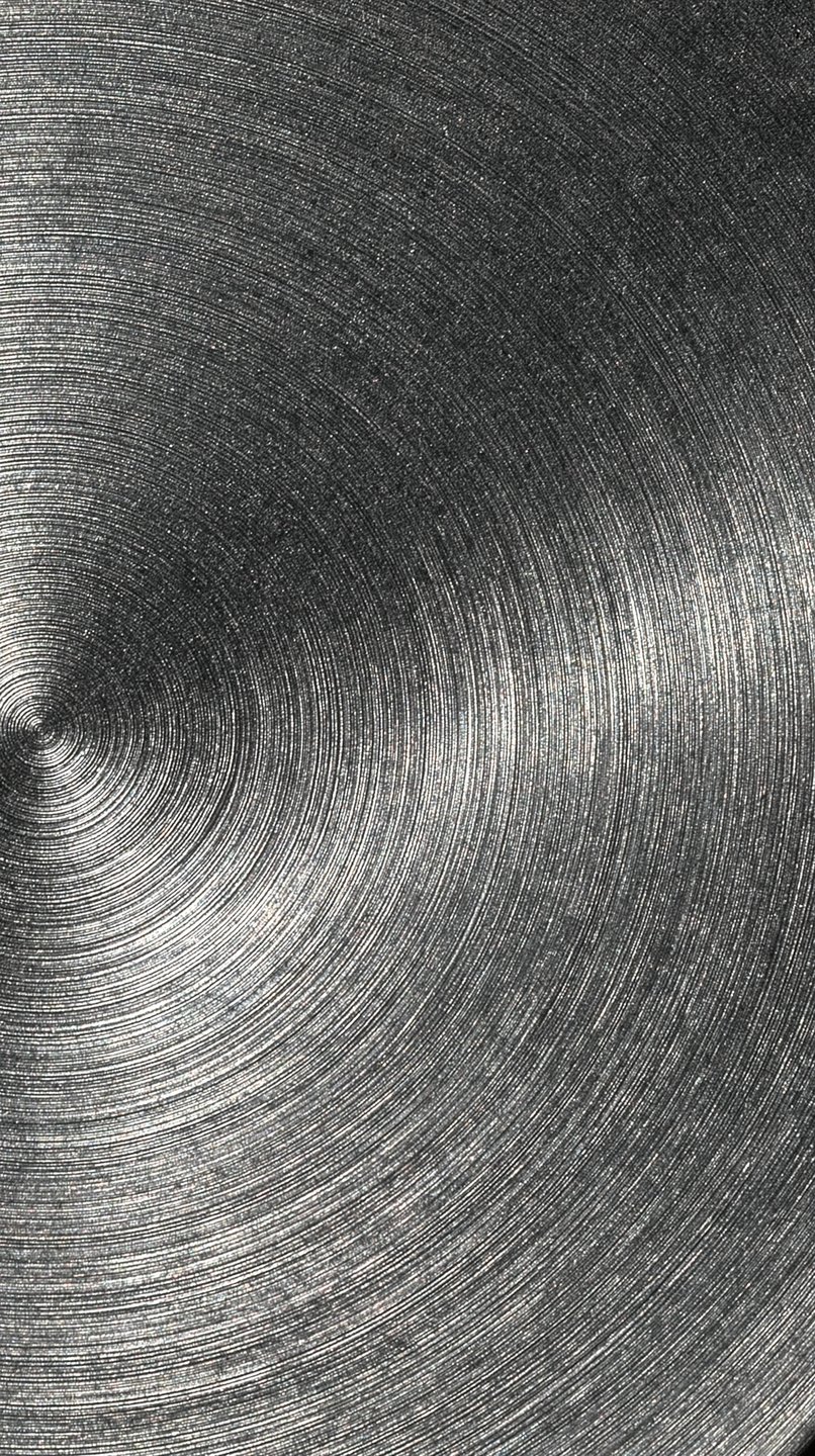 Concentric brushed metal texture with circular grooves radiating from an off-center point under bright specular light.