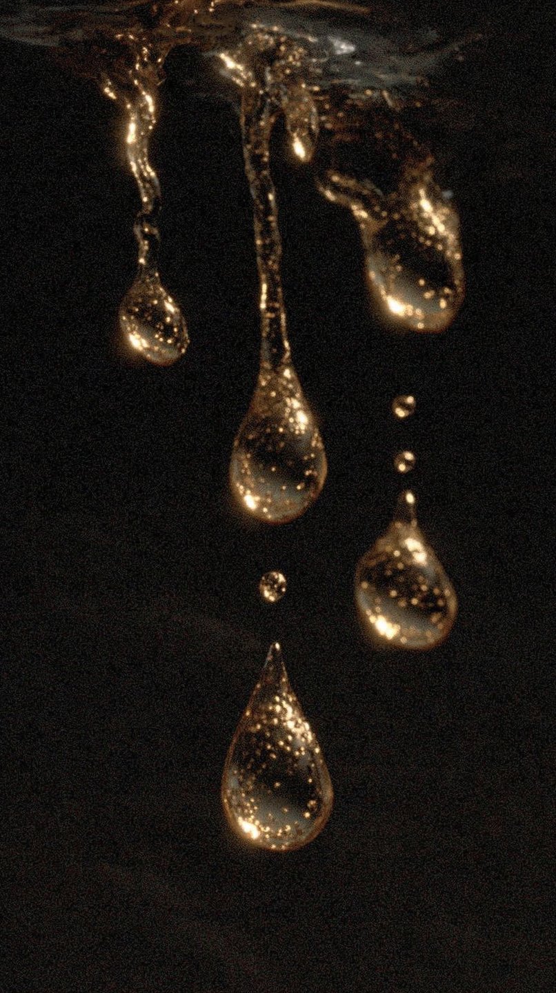 Shimmering golden liquid droplets suspended and falling against a dark, textured background with sparkling internal details.