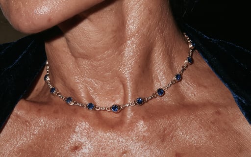 Close-up of a silver necklace with blue sapphire gemstones on a mature woman's neck with velvet clothing.