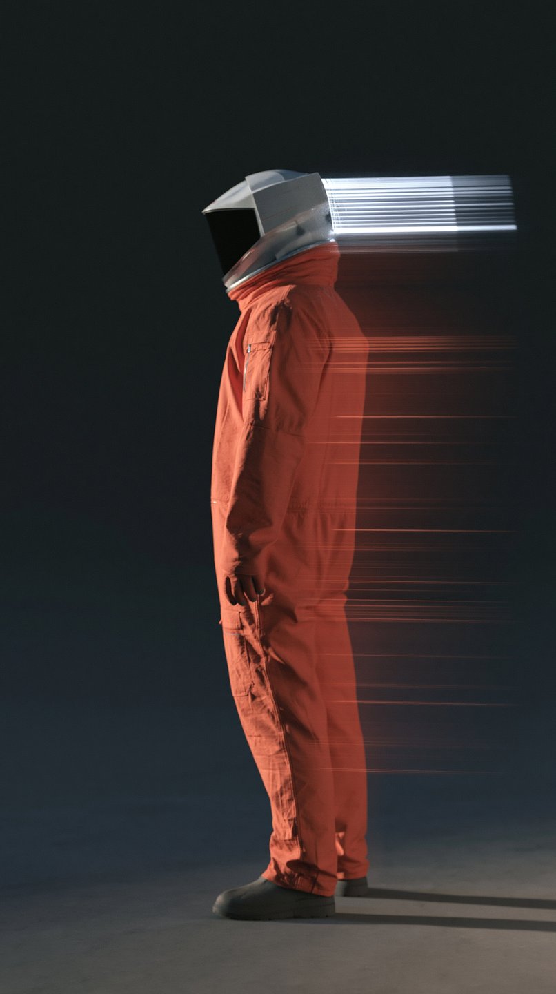 A figure in an orange jumpsuit and geometric helmet stands in profile with a horizontal motion trail.