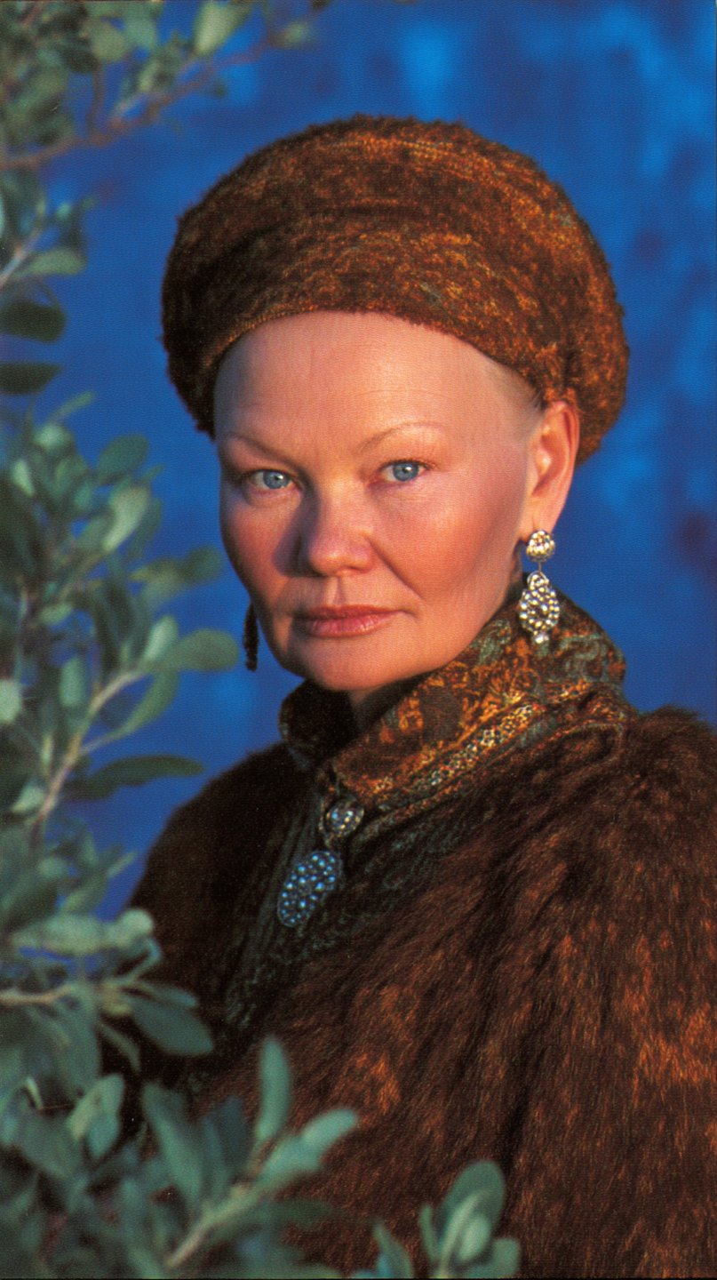 Mature woman wearing a textured ochre headpiece and fur cloak, looking forward against a blue background.