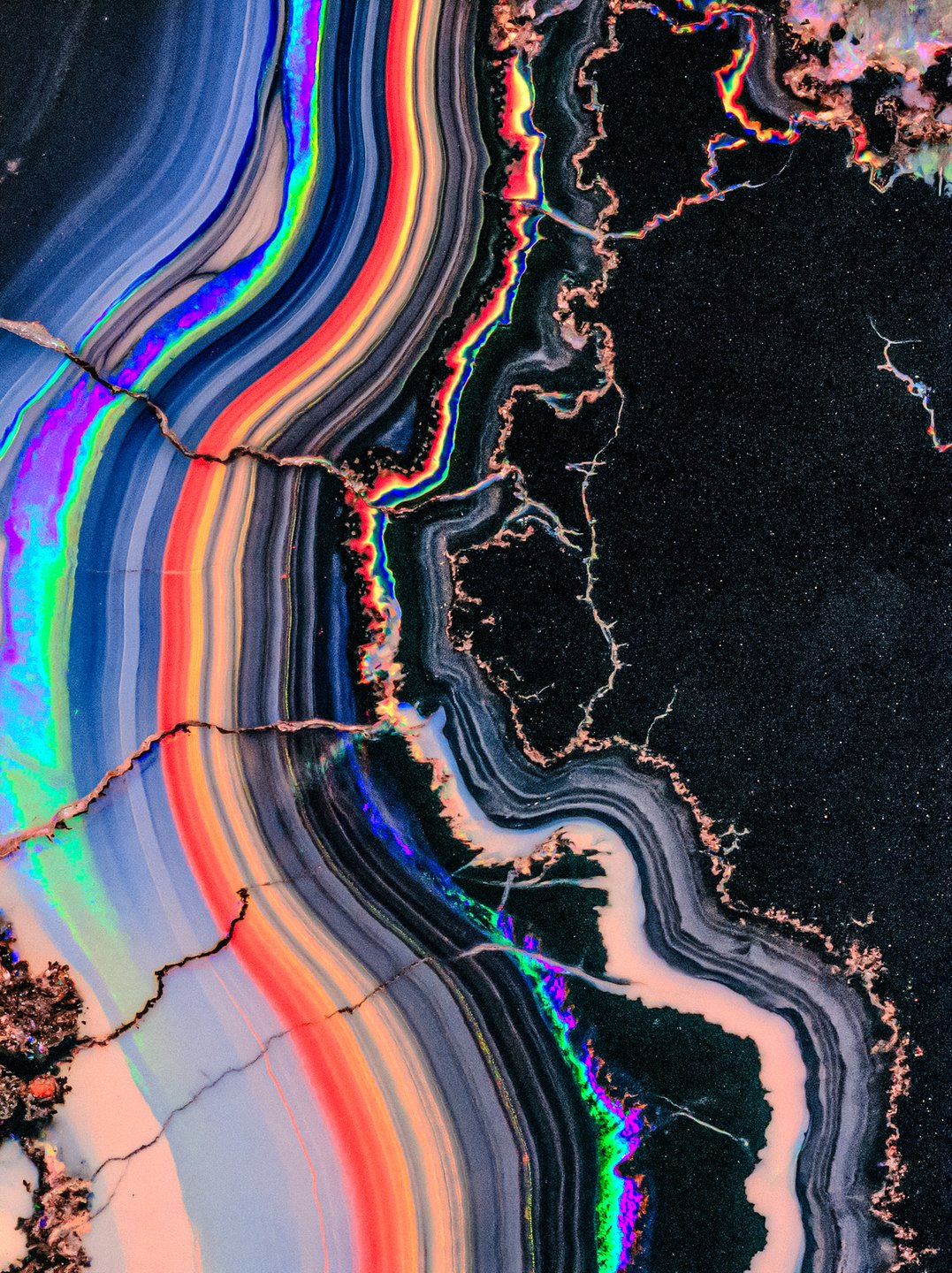 Cross-section of an agate stone featuring brilliant rainbow iridescent bands alongside a dark textured mineral matrix.