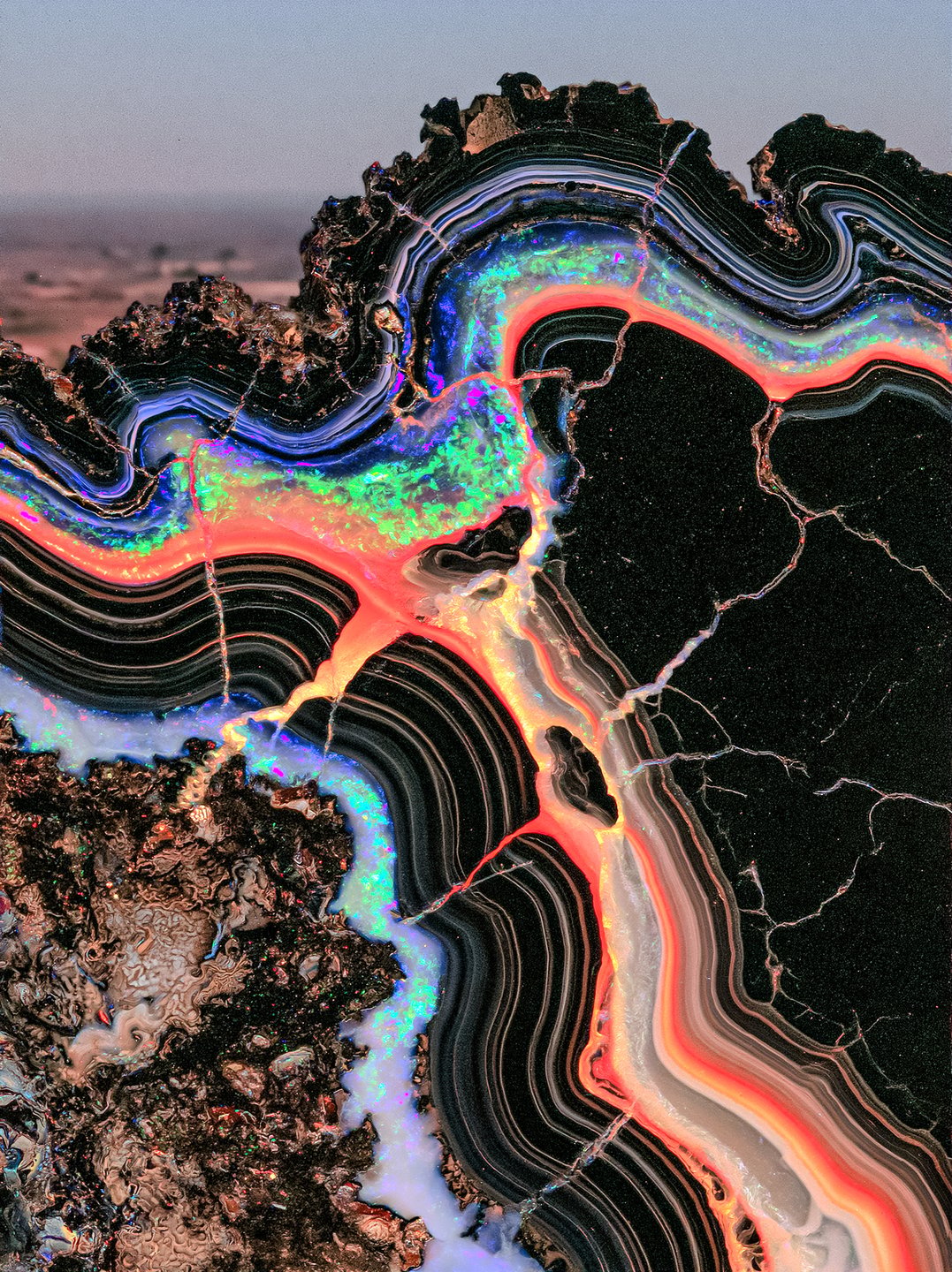 A close-up cross-section of a dark mineral geode with glowing neon pink, green, and orange iridescent bands.