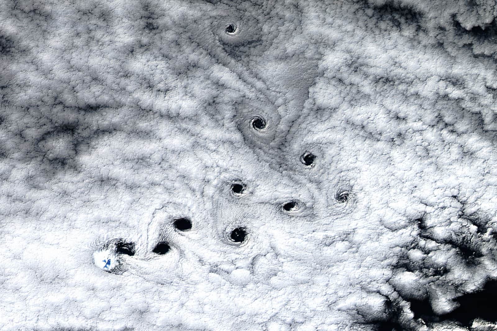 Dark round holes in a white cloud deck, in a line north of Heard Island's white peak