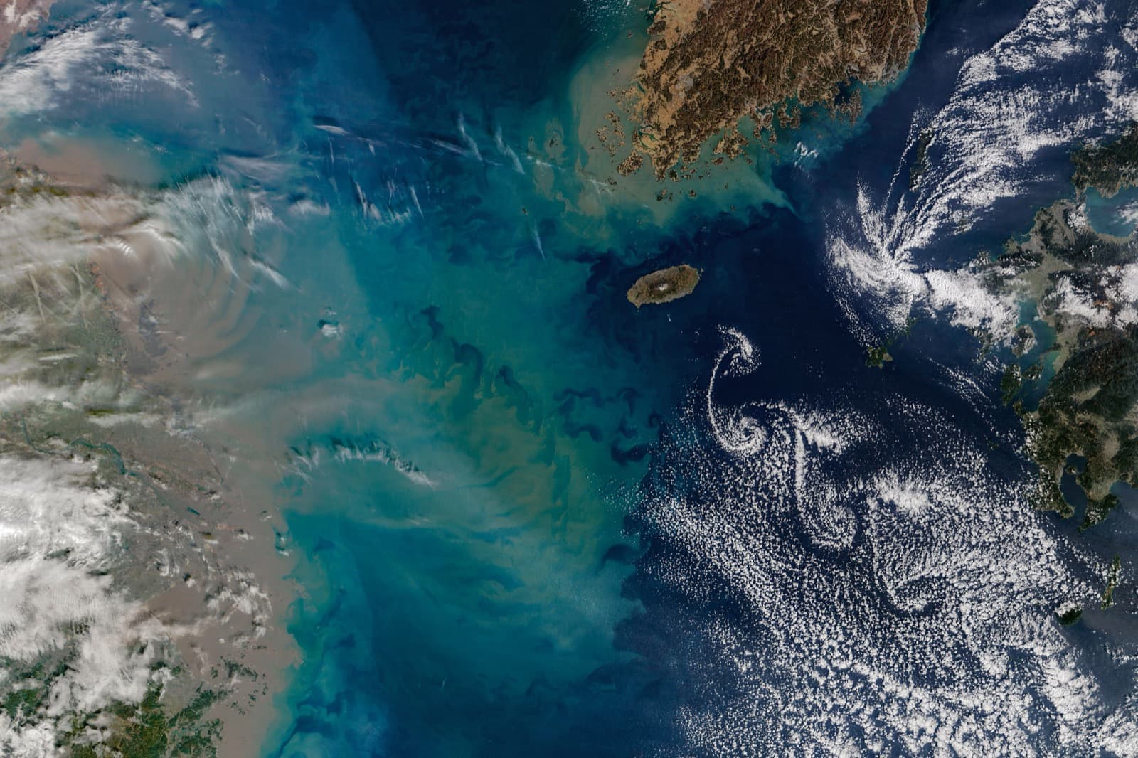Spiral clouds drifting south-east of Jeju Island over a dark blue sea