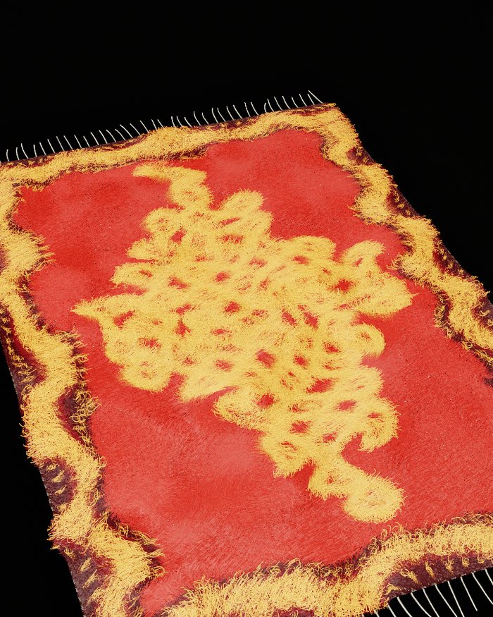 The kolam rug with carve raised, so the gold motif stands taller than the red field
